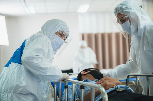 professional doctors in the full protective suits and surgical masks are examining the infected patient in the hospital control area