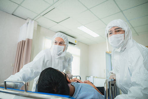 professional doctors in the full protective suits and surgical masks are examining the infected patient in the hospital control area