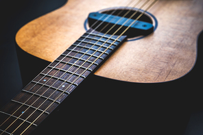 Acoustic guitar, music instrument resting against a dark black background with copy space, Close-up of wooden classic guitar