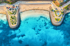 Aerial view of beautiful sandy beach, clear blue sea, promenade, swimming people in clear water, green trees at sunset in summer. Top view of seafront. Tropical landscape. View from drone of sea shore