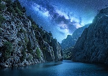 Milky Way over the beautiful mountain canyon and blue sea at night in summer. Colorful landscape with bright starry sky with Milky Way, rocks, trees, moonlight, constellation. Galaxy. Nature and space
