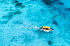 Aerial view of the fishing boat in clear blue water at sunset in summer. Top view from drone of yacht, sandy beach in Indian ocean. Travel in Zanzibar, Africa. Tropical landscape with motorboat, sea