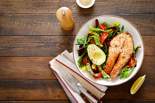 Salmon fish steak grilled, avocado and fresh vegetable salad with tomato, bell pepper and leafy vegetables. Top view