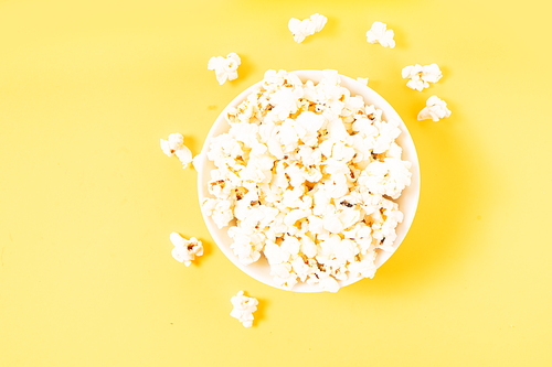 Bowl with popcorn over plain yellow desk background