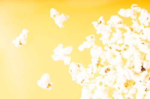 Scattered popcorn over yellow background, close up top view