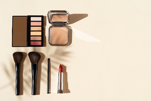 Minimal modern cosmetic scene with make up brushes, eye shadows palette, lipstick, powder and shadow overlay, top view with copy space
