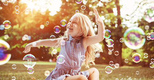 Little blond girl among lots of flying soap bubbles