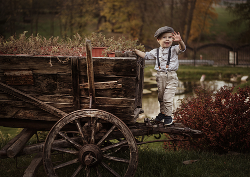 Little, cute gentleman standing on an old carriage
