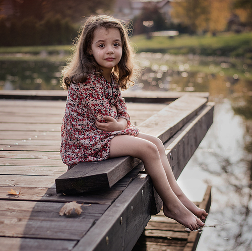 Portrait of a miserable, little girl sitting on a jetty