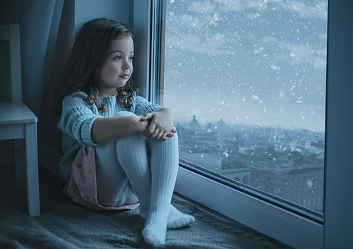Cute, little girl looking at the cityscape while snowing