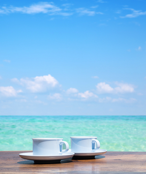 Two cups of hot coffee over a clear ocean's water