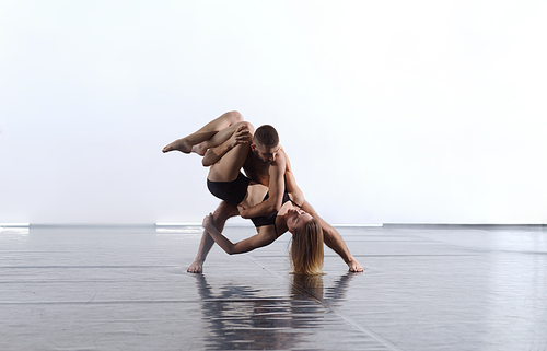 couple of young athletic dance partners in black tights performing modern style dance making acrobatic elements  couple of sporty dance dancers in art performance in front of white background