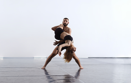 couple of young athletic dance partners in black tights performing modern style dance making acrobatic elements  couple of sporty dance dancers in art performance in front of white background