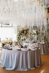 The presidium of the newlyweds in the banquet hall of the restaurant is decorated with candles and green plants, wisteria hangs from the ceiling