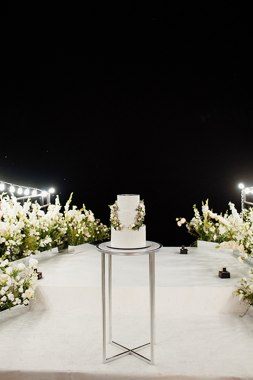 wedding white cake on a high stand near the white podium with green decor