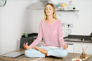 Young caucasian woman meditating in the kitchen at home