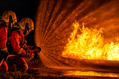 Firefighters using Twirl water fog type fire extinguisher to fighting with the fire flame from oil to control fire not to spreading out. Firefighter and industrial safety concept.
