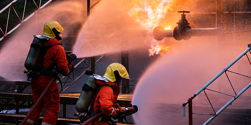Panoramic Firefighter team use water fog type fire extinguisher to fight with flame from oil pipeline leak and explosion on oil rig and natural gas station. Firefighter and industrial safety concept.