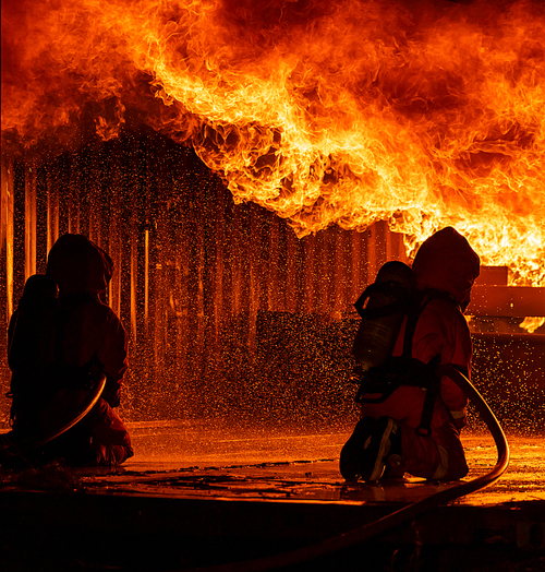 Firefighters using water fog fire extinguisher to fighting with the fire flame in large building. Firefighter and industrial safety disaster and public service concept.