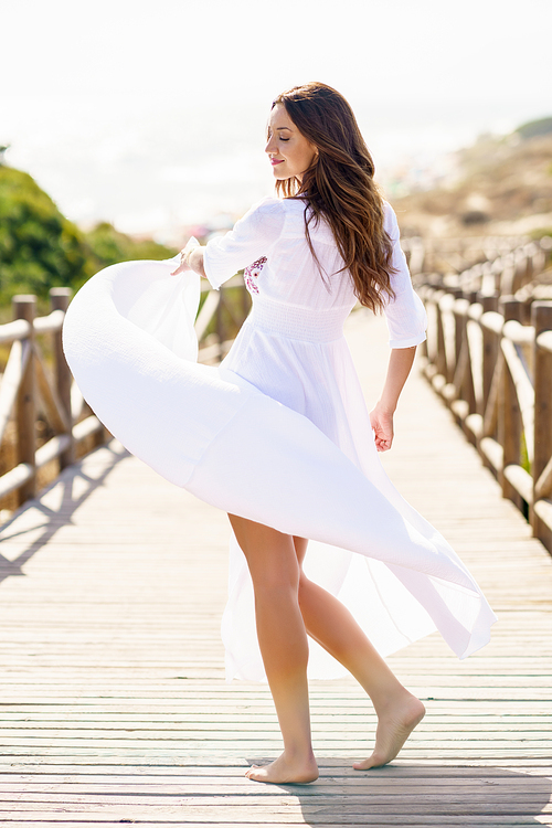 Young pretty woman moving a beautiful white dress in Spanish fashion on a boardwalk on the beach.