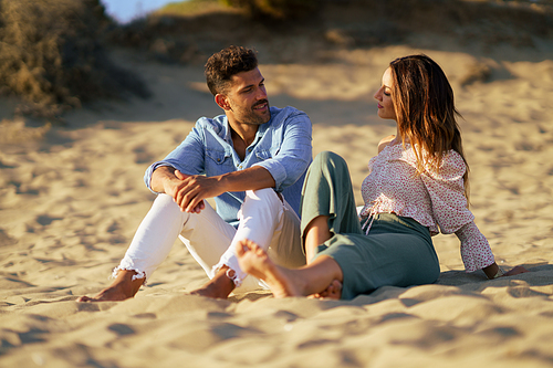 Happy loving couple sitting on the sand of the beach looking at the horizon.