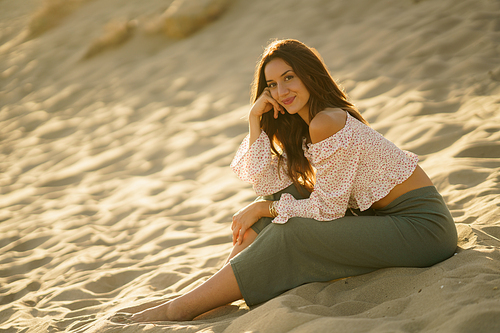 Attractive woman sitting on the sand of the beach looking at the horizon.