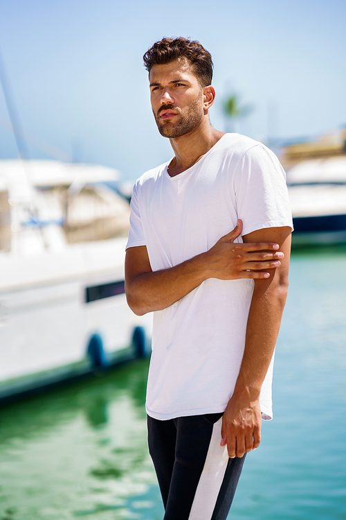 Fitness man, model of fashion, in sportswear outfit posing on waterfront harbour.