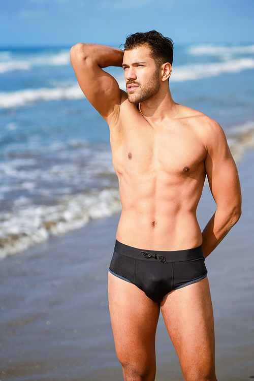 Young athletic man with fitness body standing on the sand of the beach