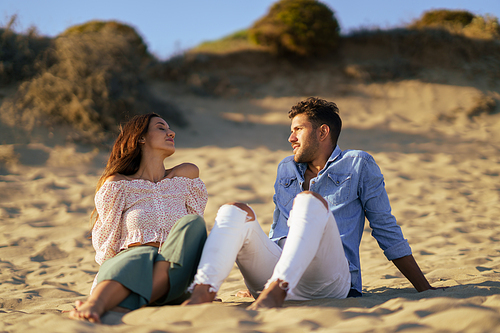 Happy loving couple sitting on the sand of the beach enjoying the tranquility