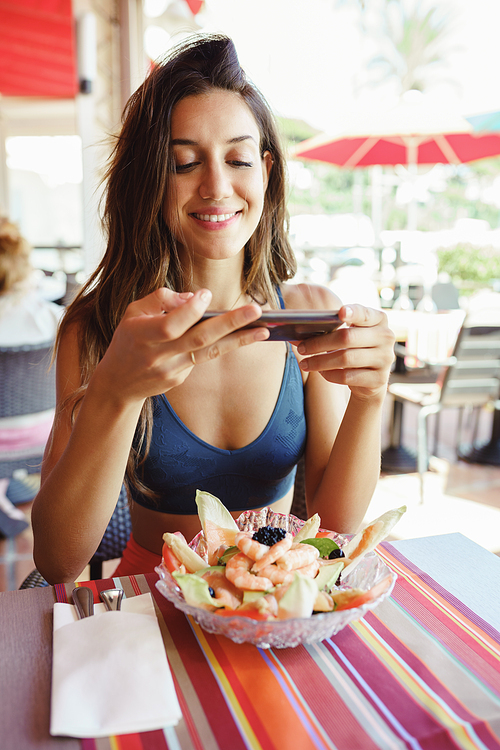 Young woman photographing her salad with a smartphone while sitting in a coastal restaurant