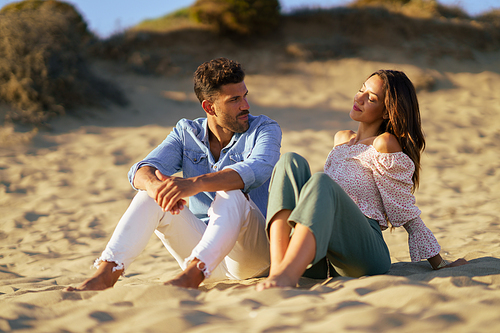 Happy loving couple sitting on the sand of the beach looking at the horizon.