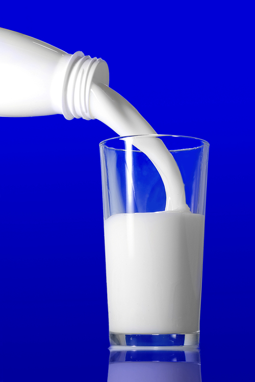 Milk pouring from bottle into glass on blue background