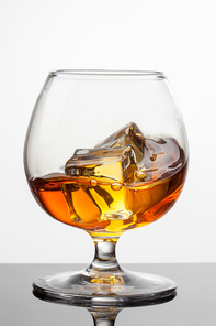 Splash of whiskey with ice in glass isolated on white. Raw image, no postproduction
