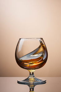 Splash of cognac in glass on brown background