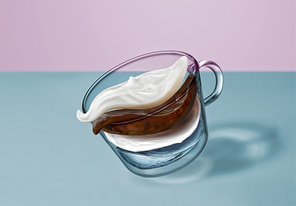 Creative composition of coffee beverage - flying layers of water, coffee, milk, creamy foam in a glass cup moving above the surface of the blue table.