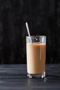 Fresh coffee with milk in a glass with a metal spoon on a black wooden table with copy space.