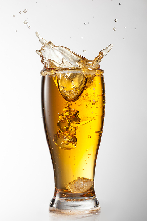 Ice falling into beer glass with splash isolated on white