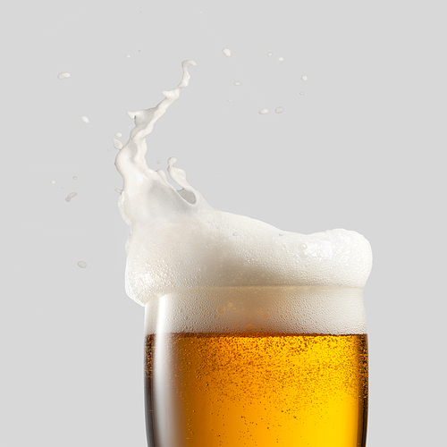 Close-up of cold beer with foam and splash on a gray background