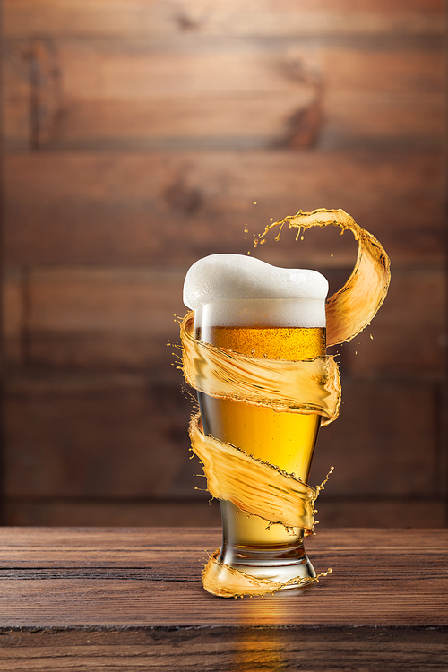 A glass of cold beer with drops and froth around a splash on a dark wooden background with copy space.