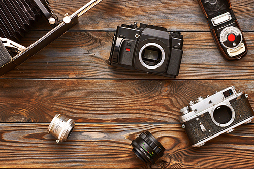 Vintage old 35mm cameras, lenses and light meter on wooden background