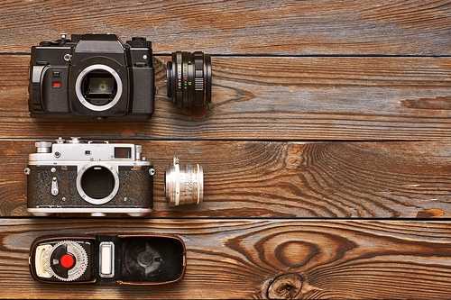 Vintage old 35mm cameras, lenses and light meter on wooden background
