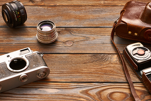 Vintage old 35mm cameras, lenses and light meter on wooden background