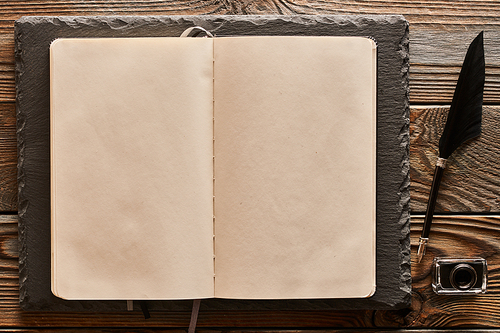 Feather pen and blank notebook page over wooden background