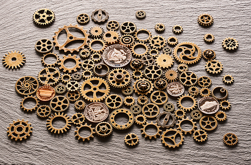 Various metal cogwheels and gear wheels with USA coins over slate background