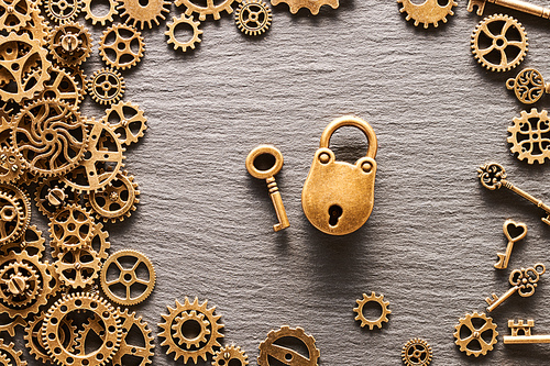 Various metal cogwheels and gear wheels with lock and key over slate background