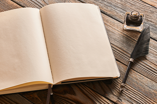 Feather pen and blank notebook page over wooden background