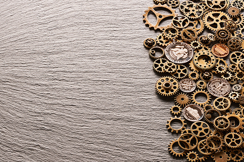 Various metal cogwheels and gear wheels with USA coins over slate background