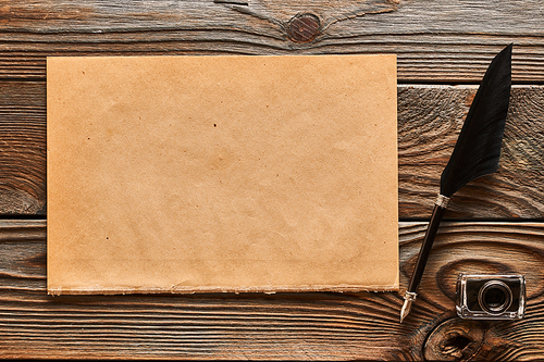 Feather pen and blank paper sheet over wooden background