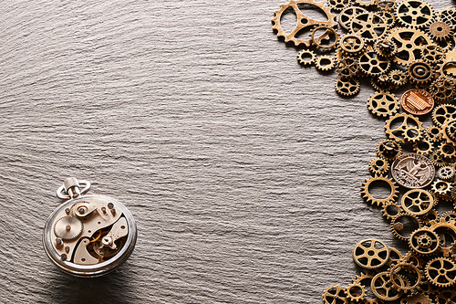 Various metal cogwheels and USA coins with clockwork over slate background