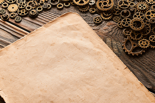 Various metal cogwheels and gear wheels with blank paper sheet over wooden background